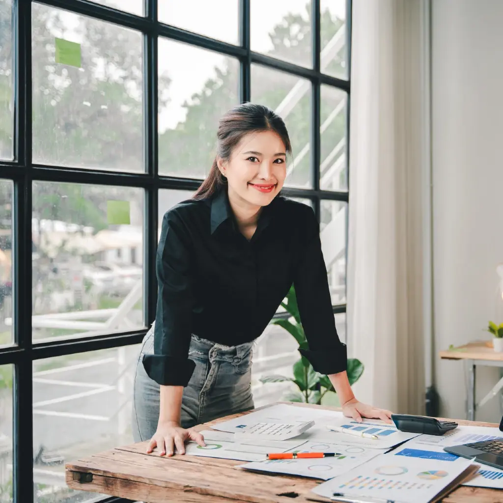 A black haired woman smiling with a table full plans and reports.