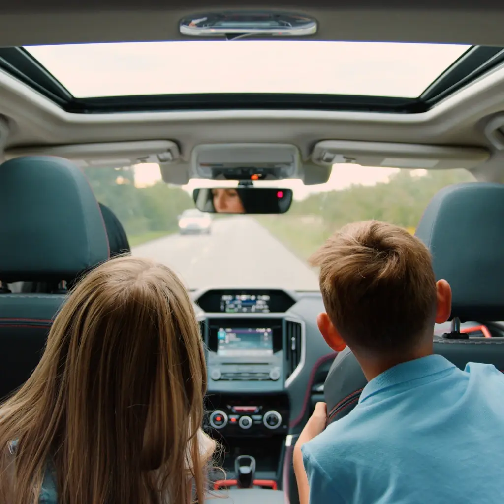Children in the backseat of a vehicle, looking forward to see the road as their mother is driving.