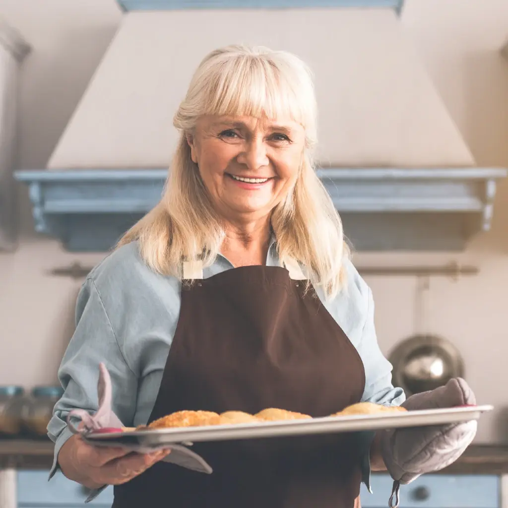 A woman in the kitchen holding a tray of pies.