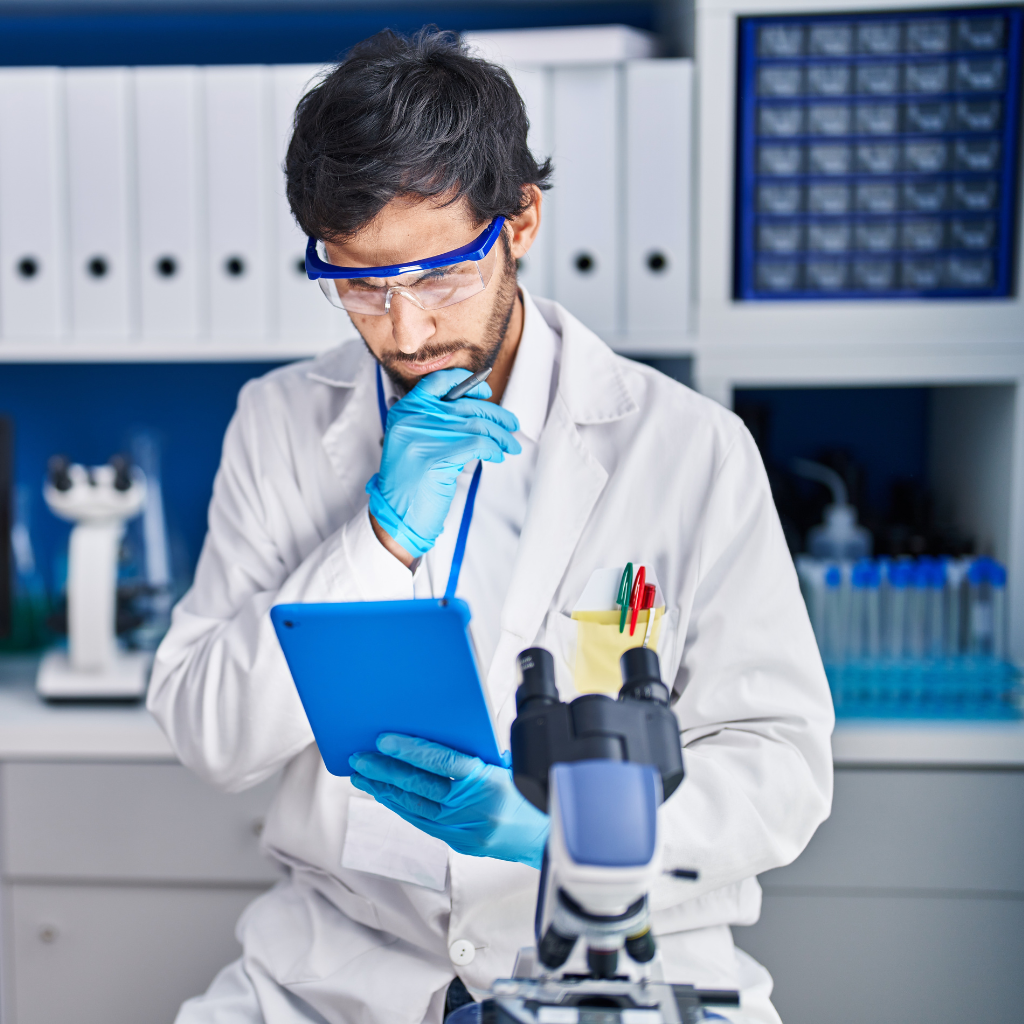 Man in a lab coat and goggles looking at a device inside a laboratory.