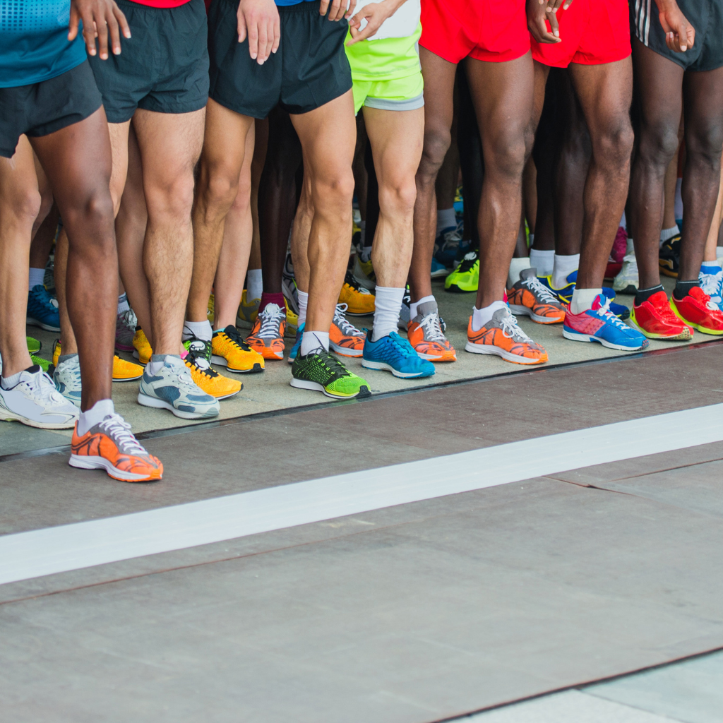 Close-up of runners' legs and colorful running shoes at the starting line of a race.