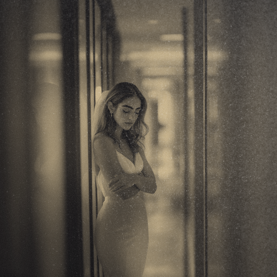 A hallway where a bride in a designer wedding gown is standing with her arms crossed and her head down.