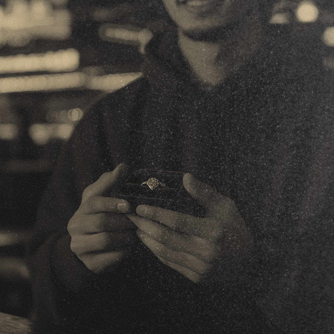 A man holding a ring box with an engagement ring inside.